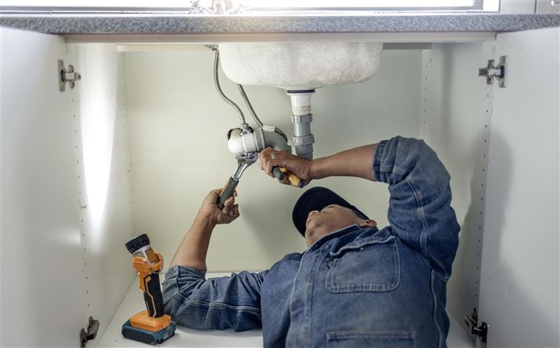 Plumber repairing pipes beneath a bathroom sink in St. Petersburg