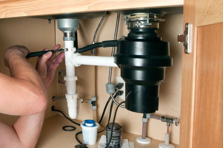 Plumber installing a garbage disposal beneath a kitchen sink in St. Petersburg